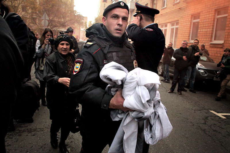 Сотрудник правоохранительных органов отбирает у участников  акции плакат в поддержку Михаила Косенко