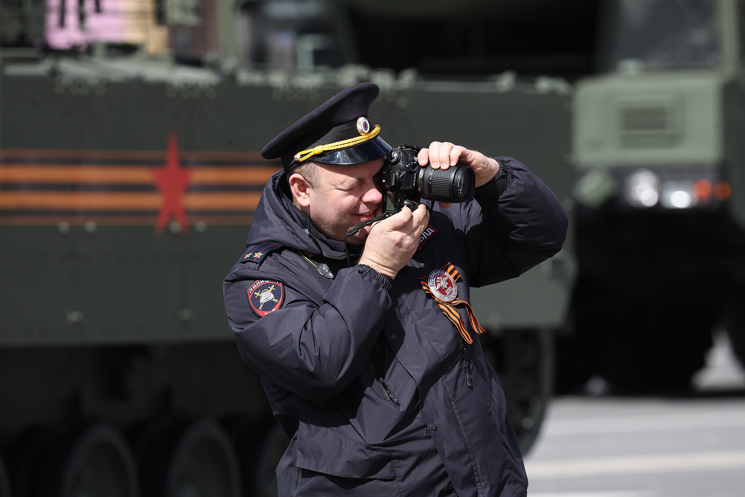 Полицейский фотографирует зрителей и образцы военной техники.