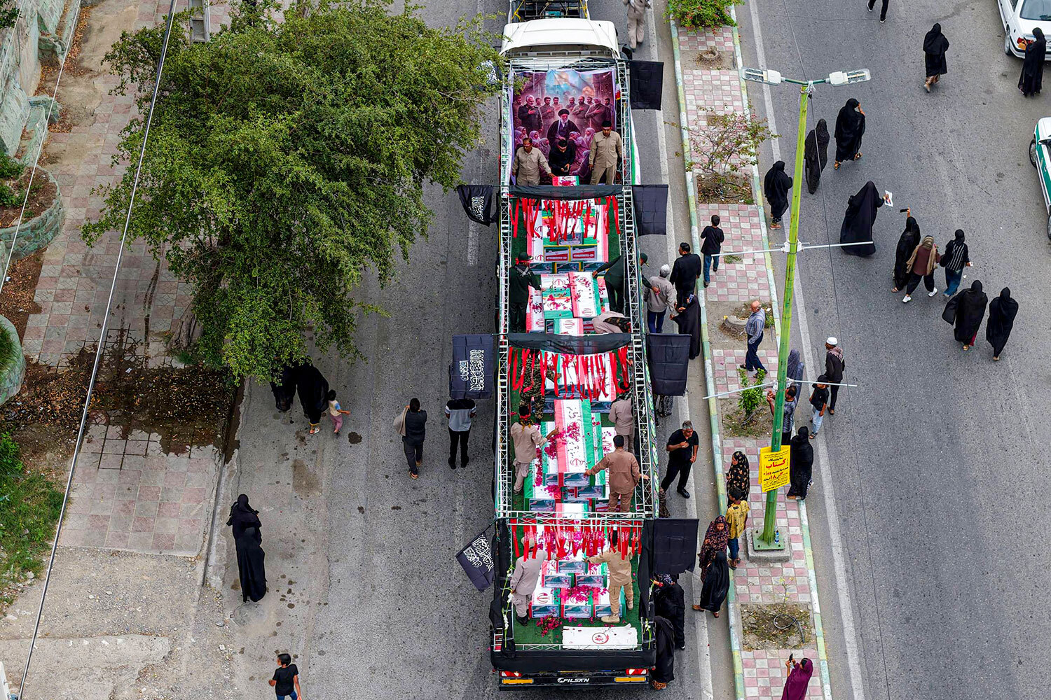 Во время похоронной процессии гробы, укрытые иранскими флагами, перевозят на грузовиках.