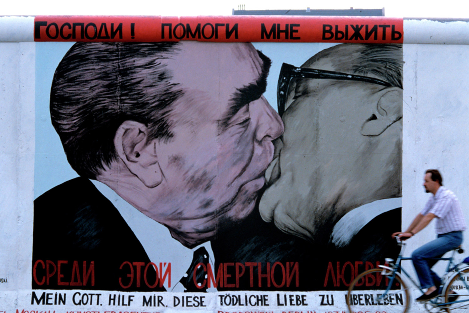 Граффити Дмитрия Врубеля «Господи! Помоги мне выжить среди этой смертной любви», известное также как «Братский поцелуй» и ставшее одним из самых узнаваемых политических арт‑образов конца XX в., украшает фрагмент Берлинской стены. В основе работы – культовый снимок 1979 г., на котором генеральный секретарь ЦК КПСС Леонид Брежнев целует руководителя ГДР Эриха Хонеккера. Врубель намеренно усилил плакатность композиции, подчеркнув гротескность «ритуального» жеста, который в эпоху соцлагеря был знаком высшего политического доверия. Созданное в 1990 г. и восстановленное автором в 2009‑м, граффити остается символом перелома эпох.